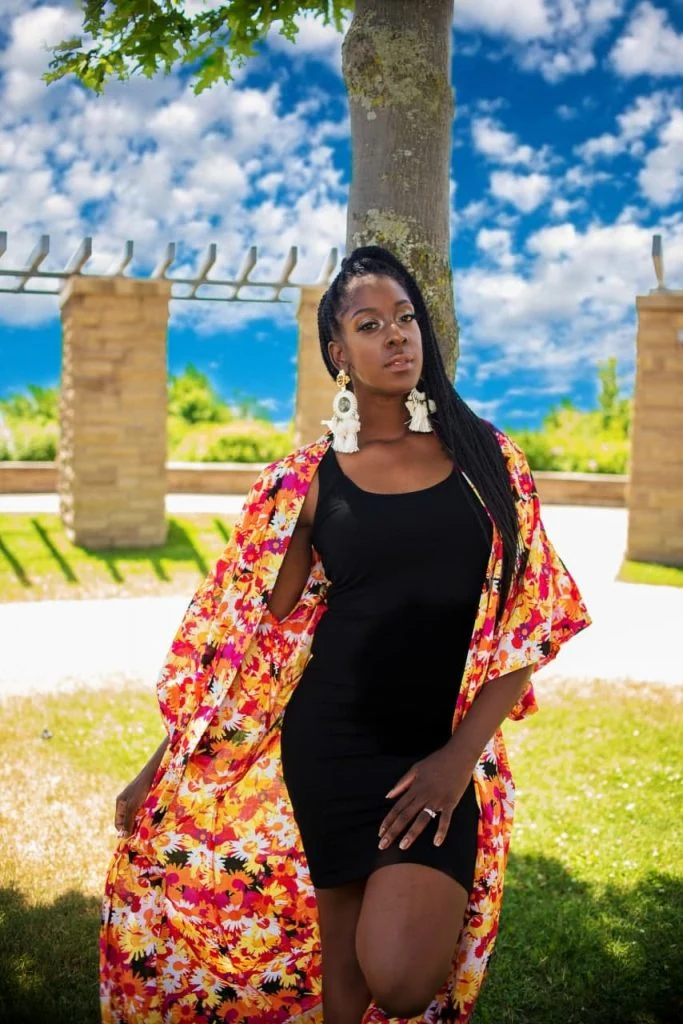 A black woman in a floral kimono posing in front of a tree.